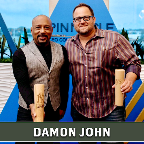 Daymond John posing beside another man, both holding wooden Dugout Mugs baseball bat mugs.