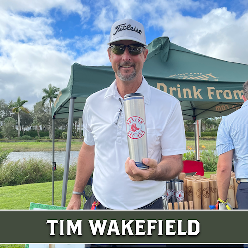 Tim Wakefield holding a baseball bat-shaped mug at an outdoor golf event.